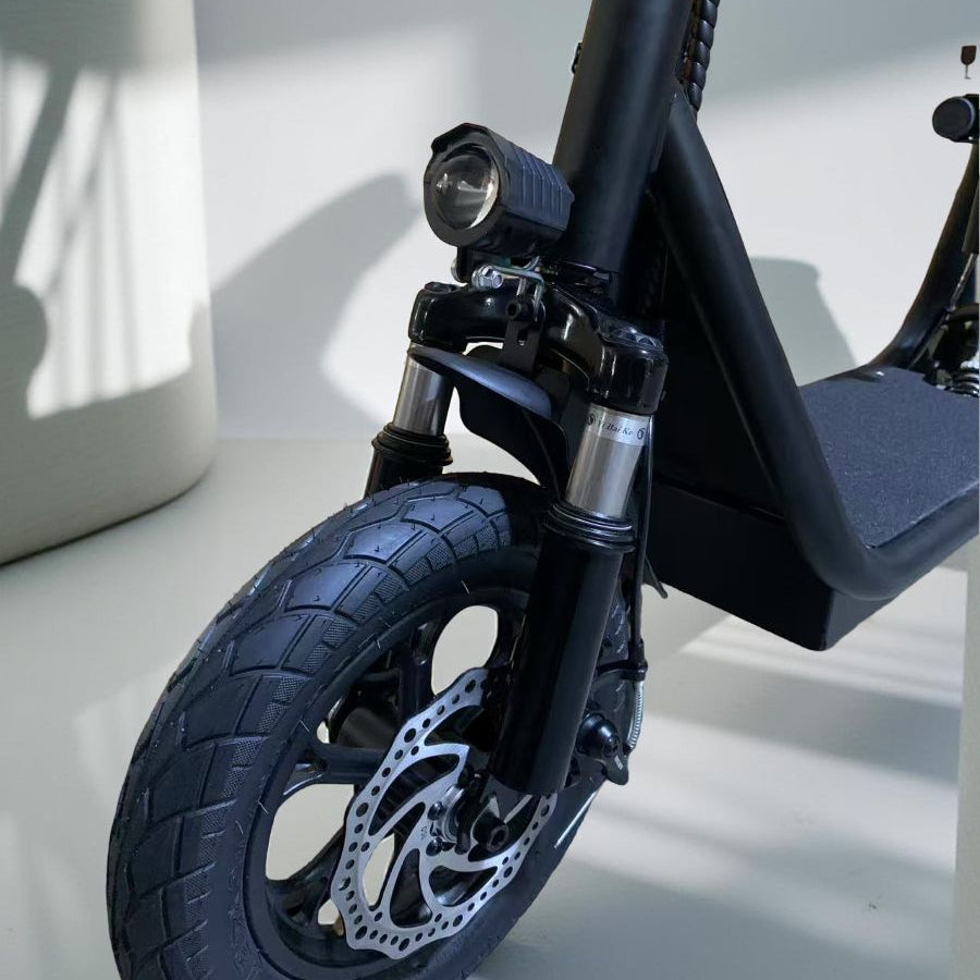 Close-up of a black electric scooter's front wheel and suspension on a light background