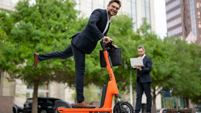 E-scooter vs petrol scooter - Man in corporate attire riding an electric scooter