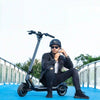 Man sits on the deck of his Punk rider 600. Location shot on a blue footbridge. This is a Water resistent electric scooter. Electric Scooter Shop, Auckland