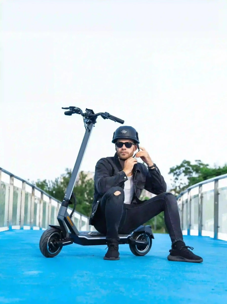 Man sits on the deck of his Punk rider 600. Location shot on a blue footbridge. This is a Water resistent electric scooter. Electric Scooter Shop, Auckland