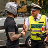 Policeman in a high-visibility vest interacting with a person wearing a helmet outdoors.