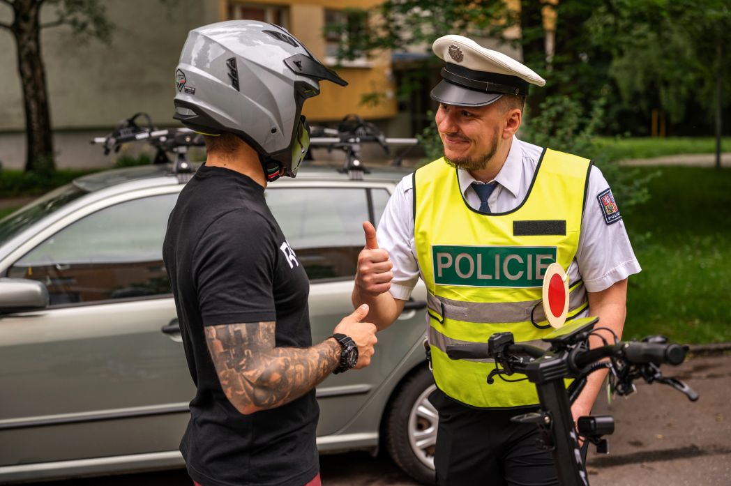 Policeman in a high-visibility vest interacting with a person wearing a helmet outdoors.