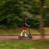 Person riding a Teverun Fighter 11 electric scooter on a path surrounded by greenery