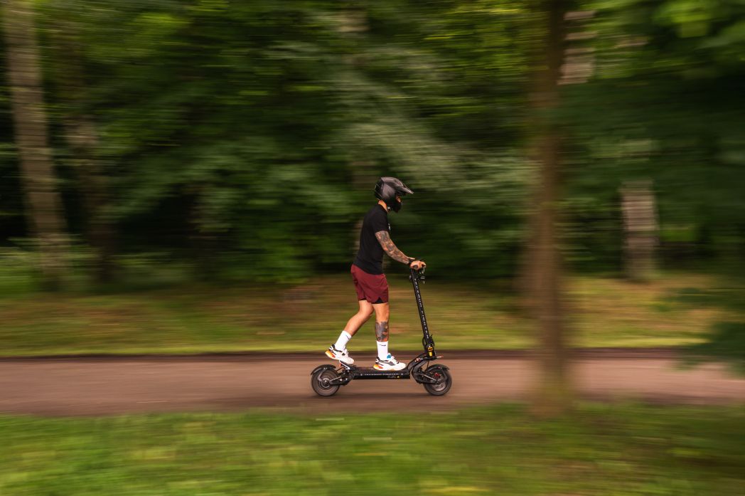 Person riding a Teverun Fighter 11 electric scooter on a path surrounded by greenery
