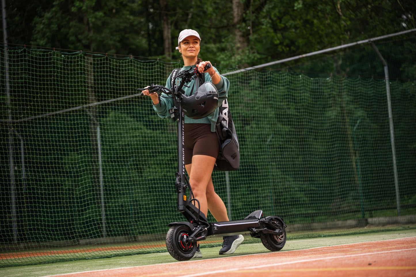 Person riding a Teverun fighter Mini  electric scooter on a track with a forest background