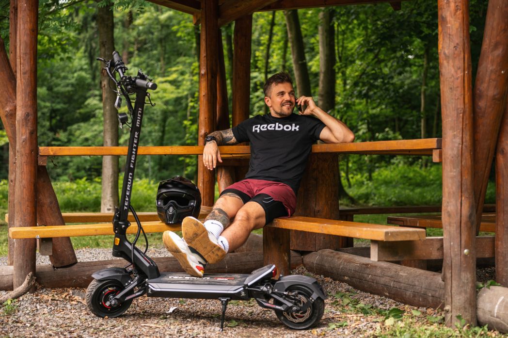 Man sitting on a wooden bench with a teverun fighter mini electric scooter in a forest setting