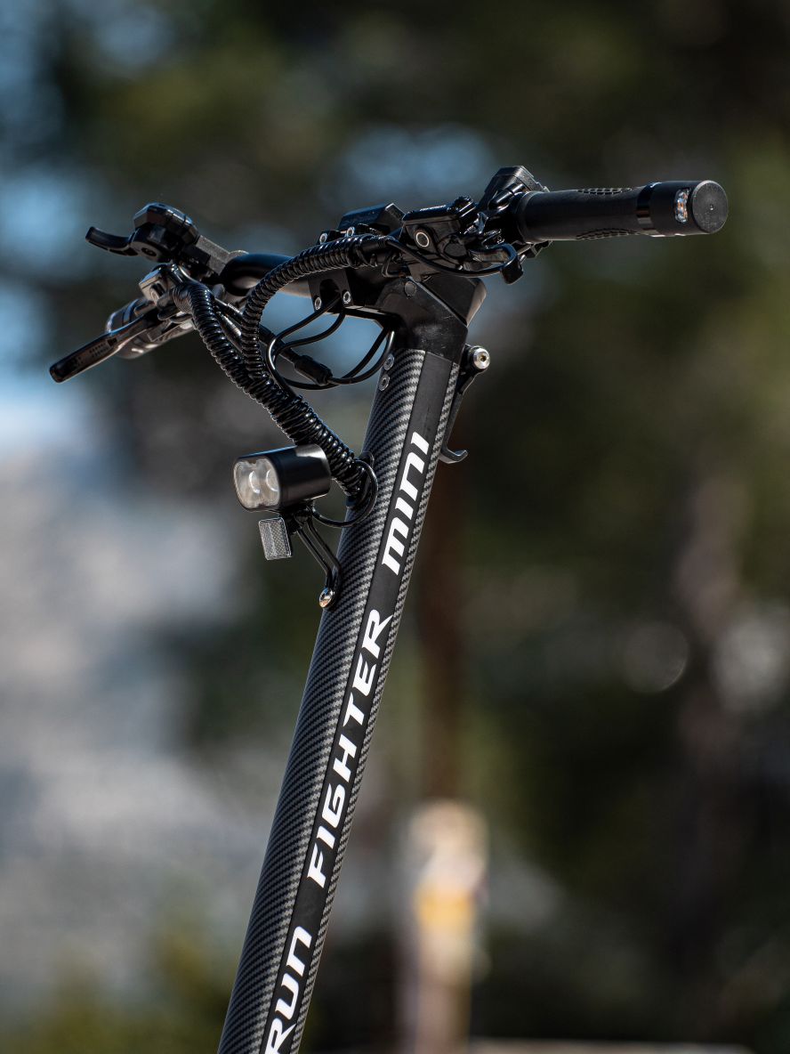 Close-up of a Teverun fighter Mini  e scooter handlebar with 'Run Fighter Mini' branding against a blurred natural background.