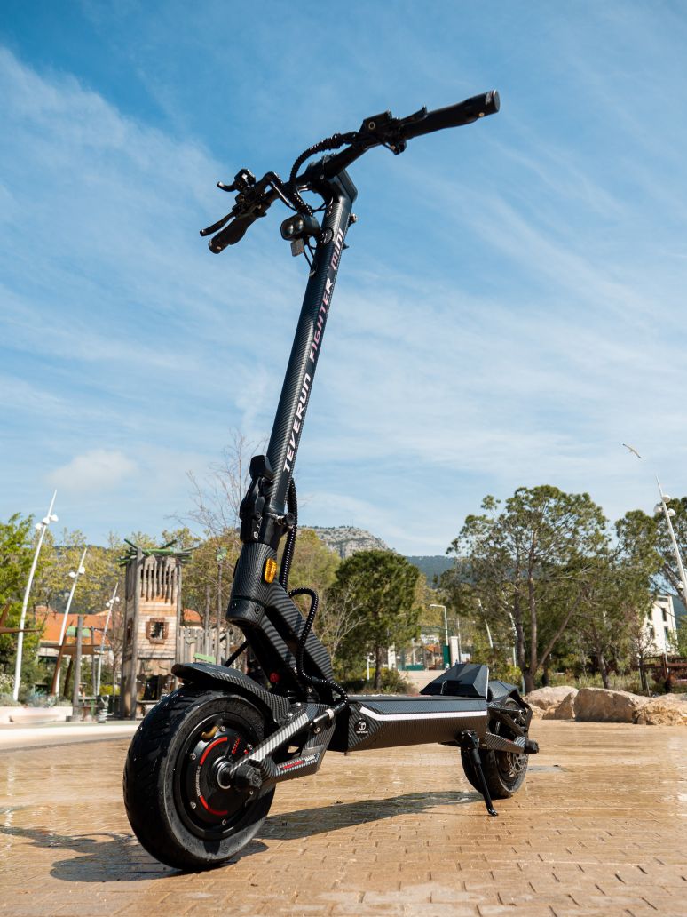 Teverun fighter Mini  Electric scooter on a paved area with trees and clear sky in the background