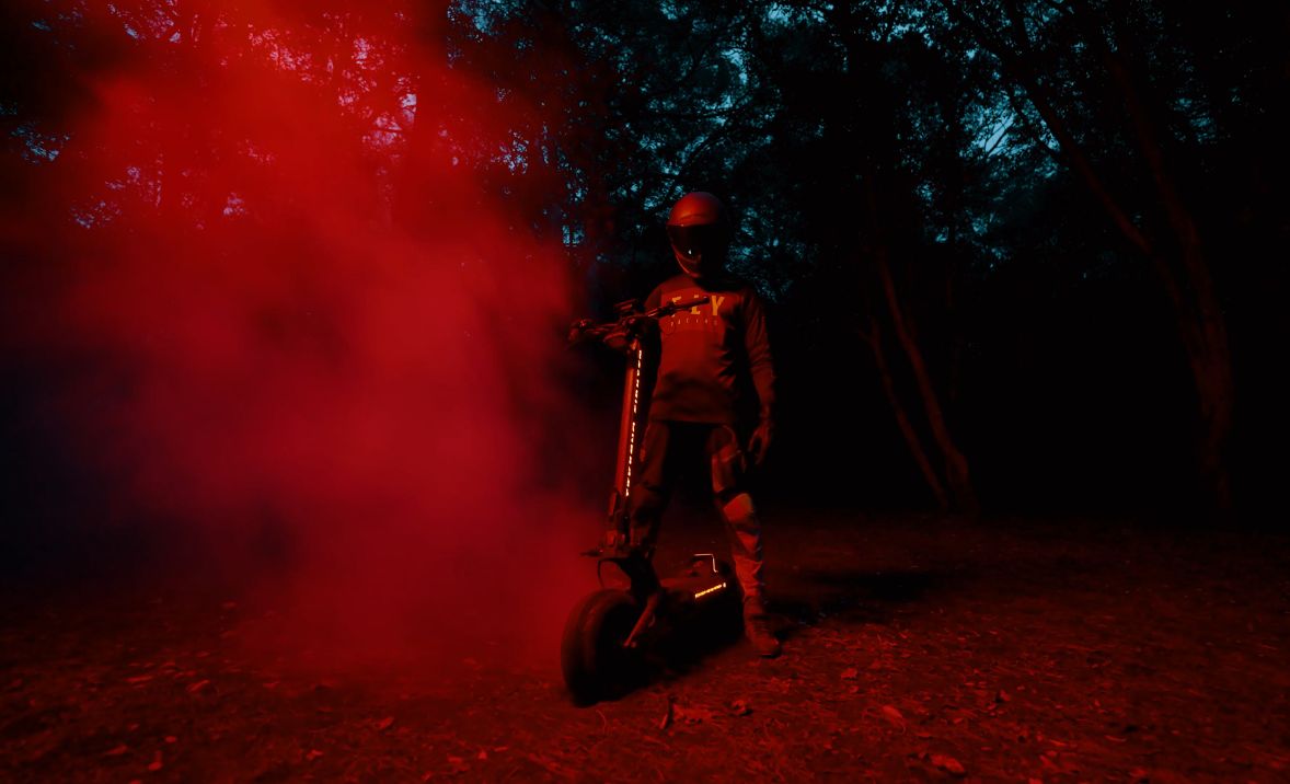 Person on a Teverun Fighter Supreme Ultra electric scooter with red smoke in a dark forest setting